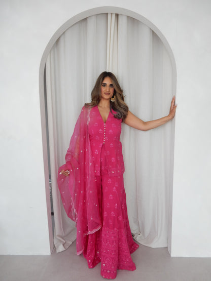 Indian Woman in a halter neck hot pink shararah standing behind a white arch way. Ideal for a jaggo or Mendhi event.