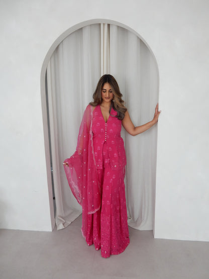 Indian Woman in a halter neck hot pink shararah standing behind a white arch way. Ideal for a jaggo or Mendhi event.